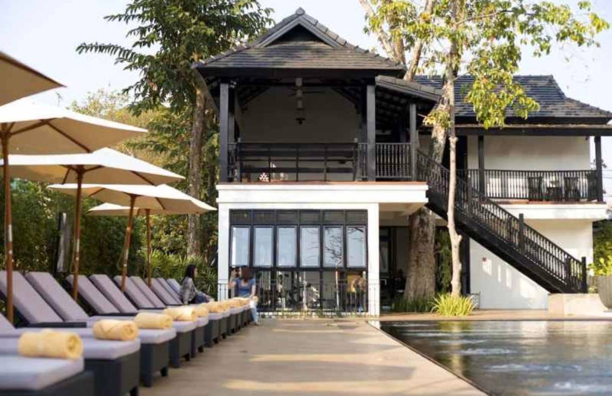 Modern black-and-white luxury pool villa with sun loungers under tropical canopy.